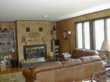 Living room portion of 2nd floor living room/dining room area with wood burning fireplace - triple windows on right provide almost full wall of pine forest view